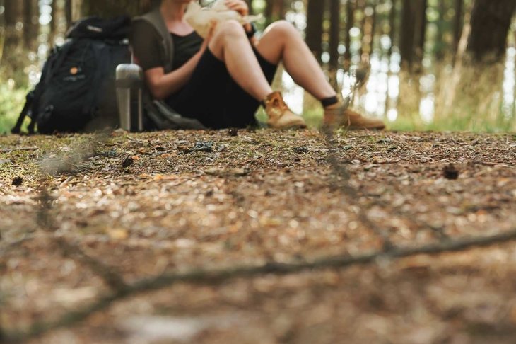 Woman hiker sitting in forest. Camera focus on the ground.